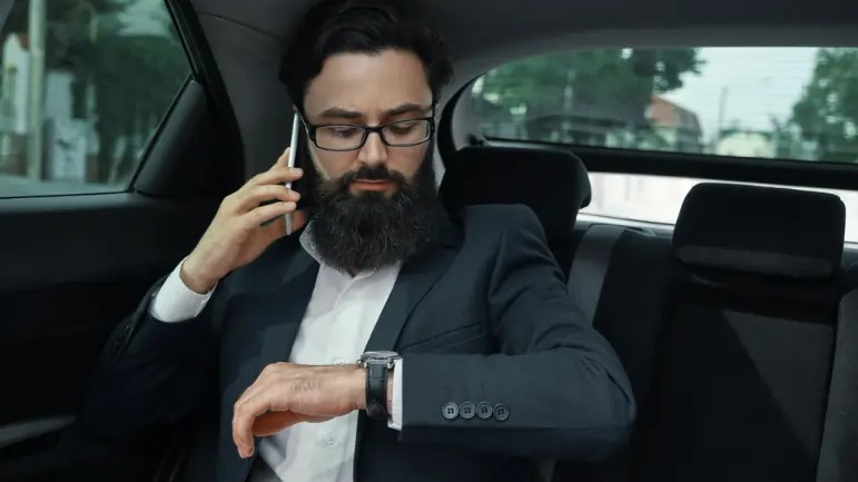 Business professional checking the time while on a phone call in a car, highlighting the importance of buffer time in event transportation Dubai.