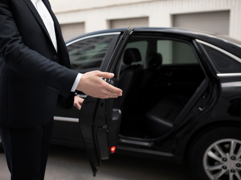 Professional driver welcoming passenger with open car door beside premium sedan in Abu Dhabi